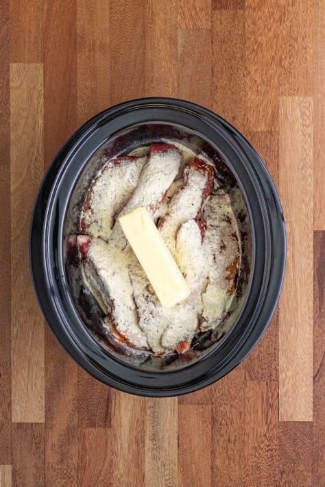 Ribs with seasoning and a stick of butter in a slow cooker.