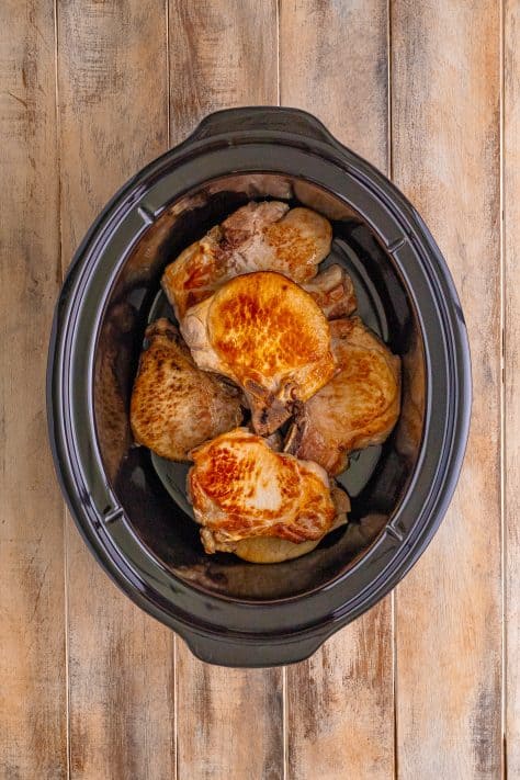 A slow cooker with seared pork chops.