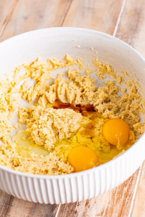 Mixing bowl with butter, white sugar, brown sugar, vanilla extract, and eggs being mixed together.