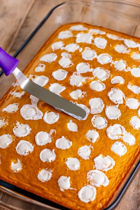 A spatula smoothing out the frosting in a Twinkie Poke Cake.