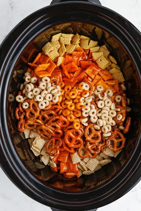A slow cooker with all the ingredients for Buffalo Ranch Chex Mix.