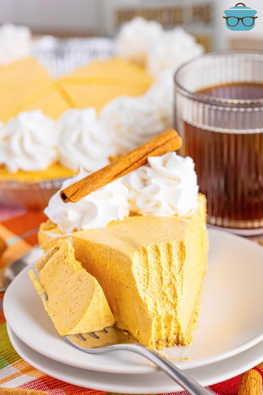 A fork holding a bite of No Bake Pumpkin Cheesecake next to the rest of the slice on a plate.