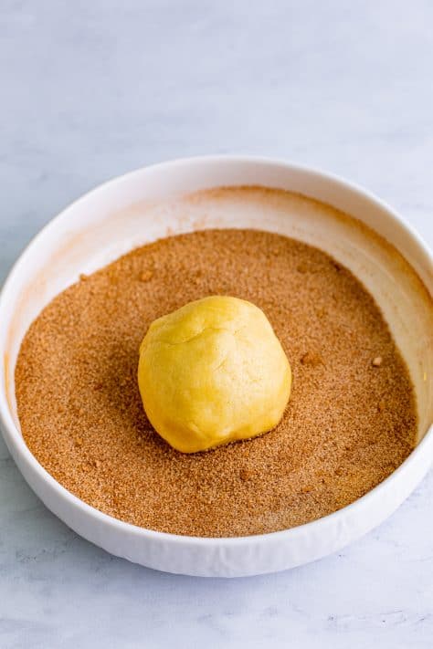 A cookie dough ball in a bowl of cinnamon sugar.