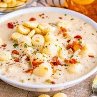 A creamy clam chowder bowl of soup with oyster crackers on top.