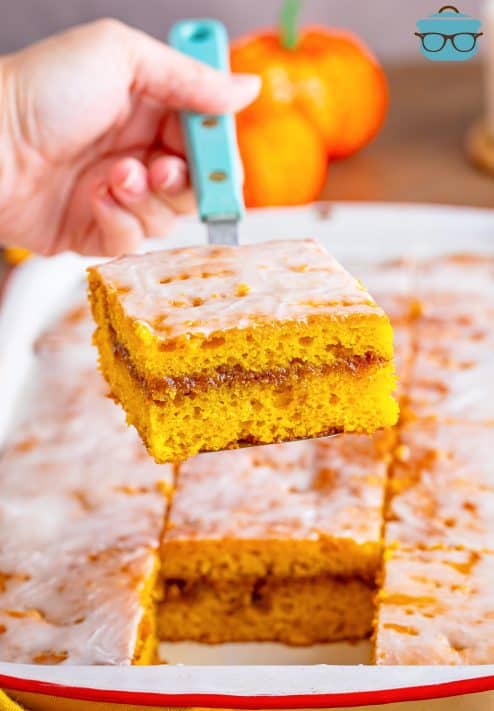 A serving utensil holding a slice of Pumpkin Honey Bun Cake over the cake.
