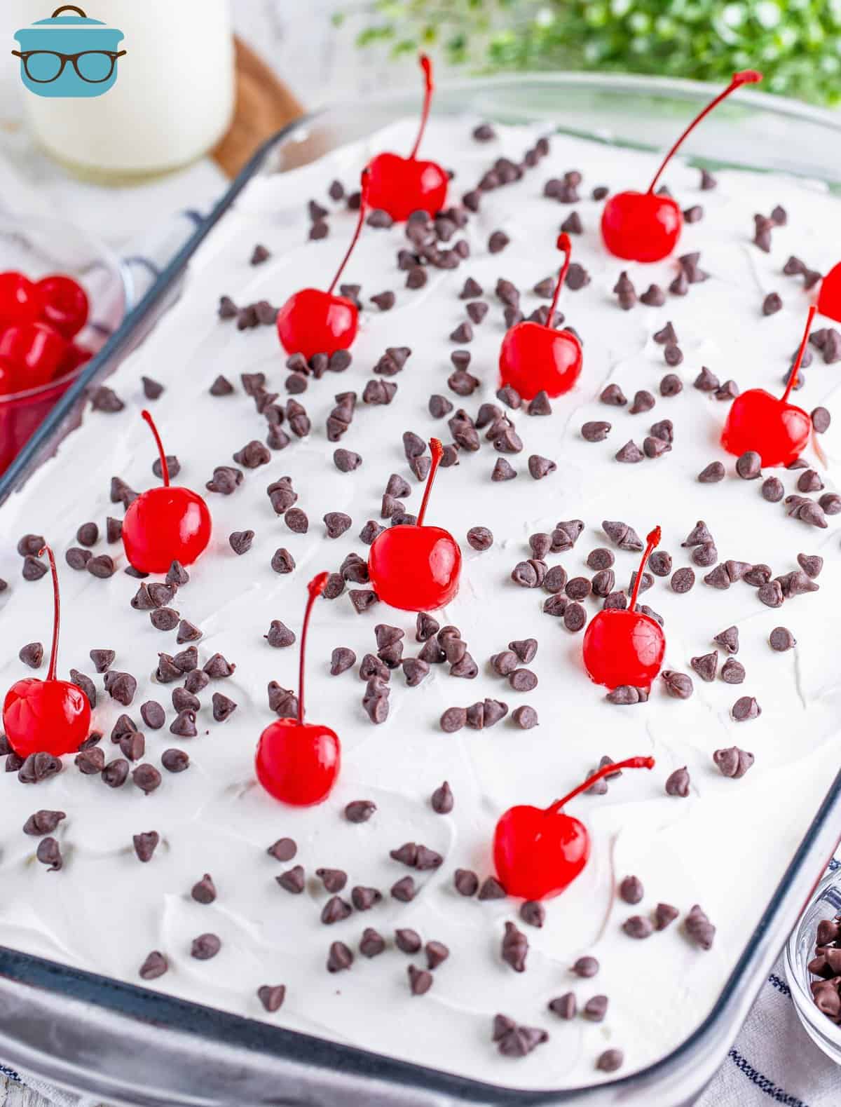 A Black Forest Poke Cake in the baking dish with chocolate sprinkles and cherries.