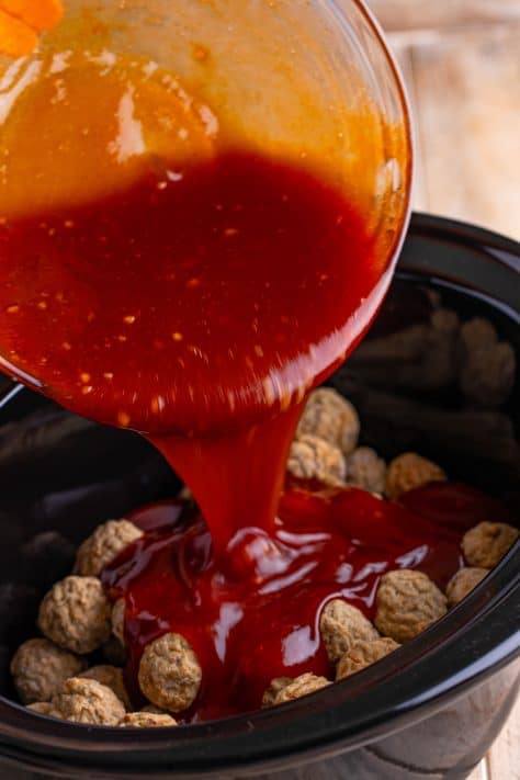 Sauce being poured over meatballs in a Crock Pot.