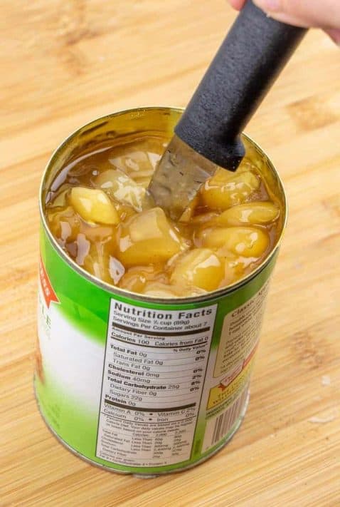 A knife cutting through the apples in the can of apple pie filling.
