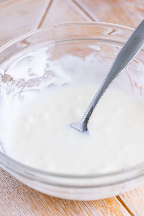 Powdered sugar and milk glaze in a small glass bowl with a spoon.
