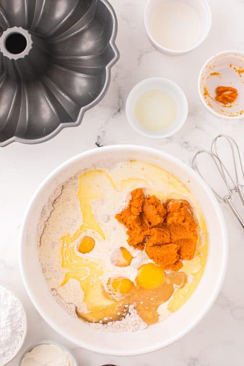 A mixing bowl with cake mix, pumpkin spice, pumpkin puree, heavy cream, melted butter, and eggs.