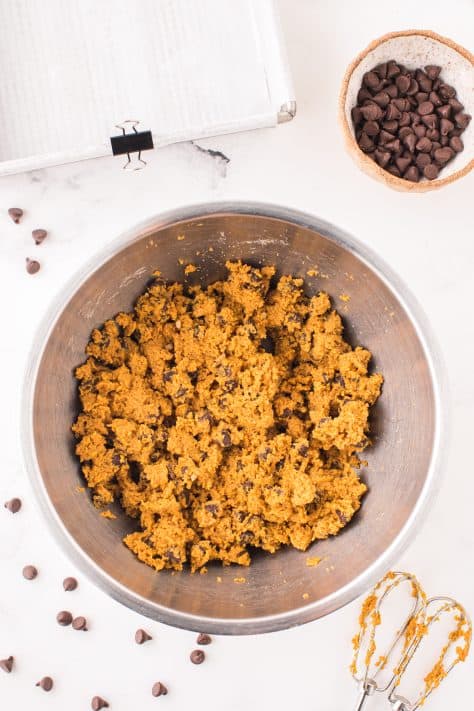 Pumpkin puree mixed into cookie douhg in a mixing bowl.