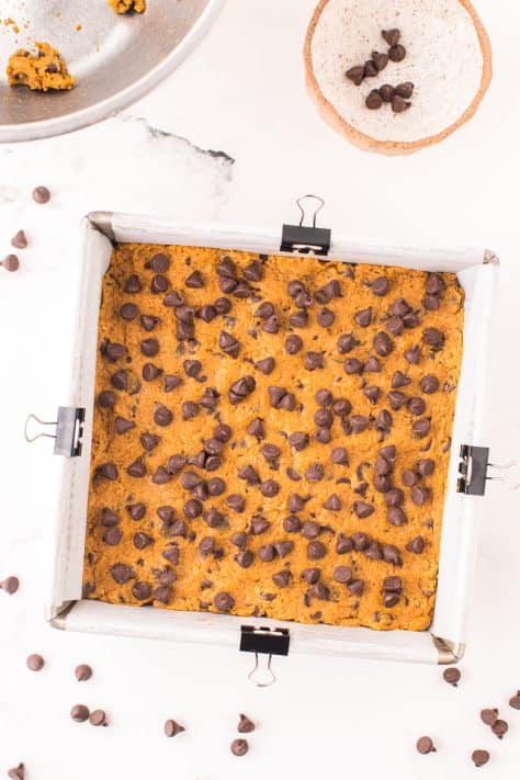 Chocolate chips sprinkled on top of cookie bar dough in a baking dish.