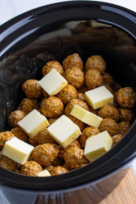 Cubed butter on top of meatballs in a slow cooker.