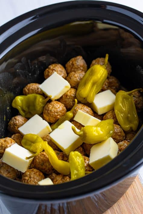 Cubed butter and pepperoncinis on top of meatballs in a Crock Pot.