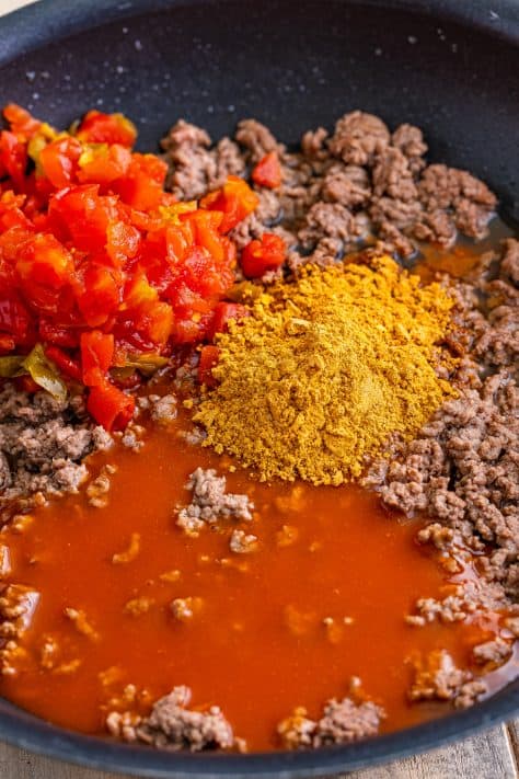 A skillet with ground beef, taco seasoning, enchilada sauce, and diced tomatoes with green chiles.