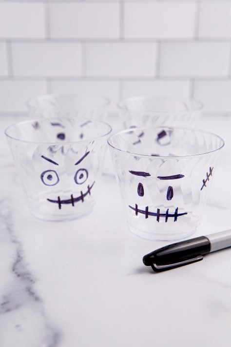 Plastic cups with Frankenstein faces drawn on them with marker.