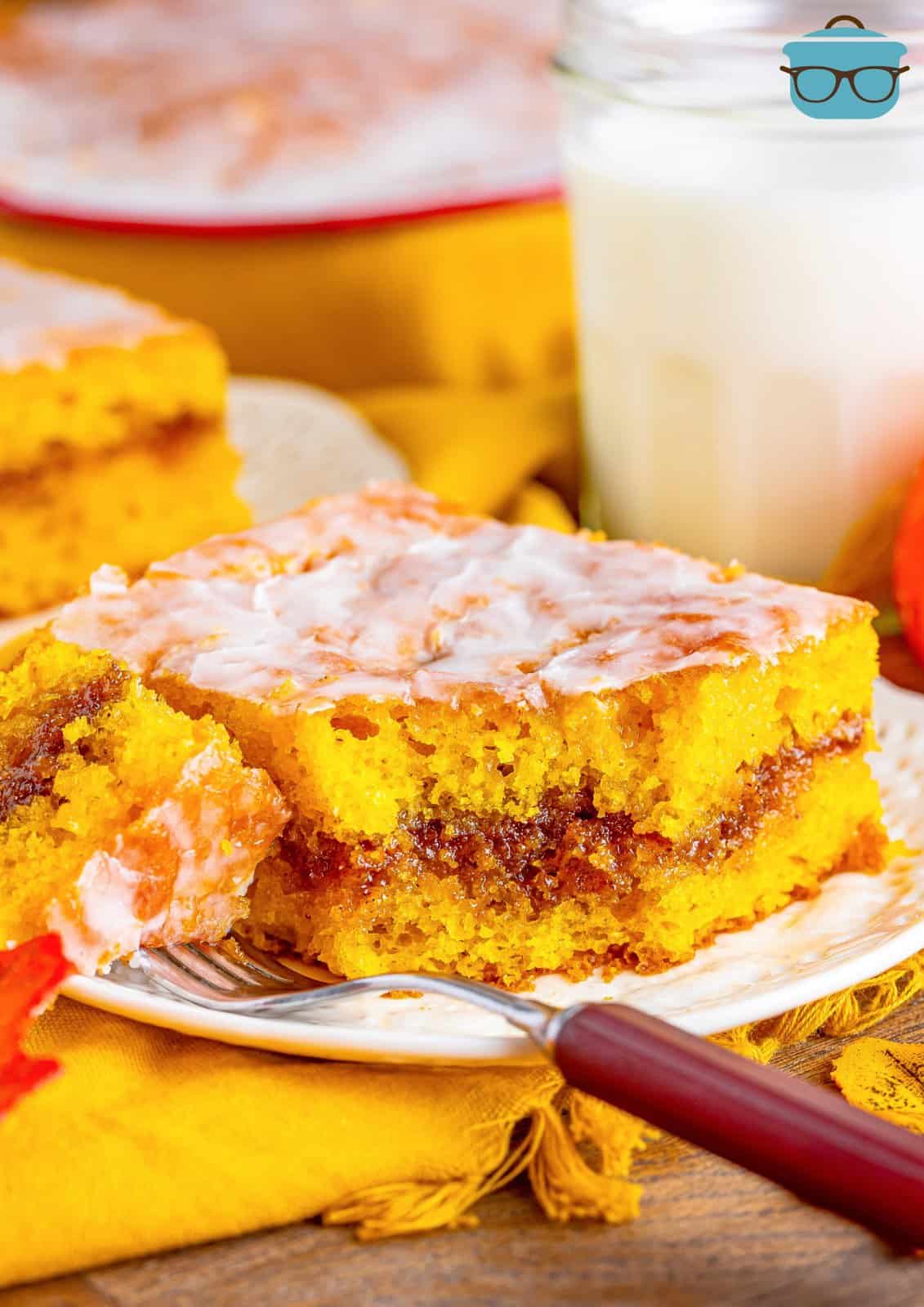 A slice of Pumpkin Honey Bun Cake on a serving plate with a bite on a fork.