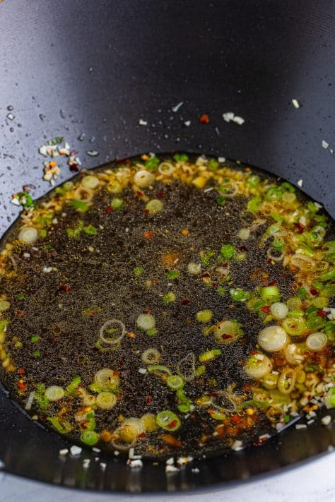 A skillet with oil, green onion, red pepper flakes, chicken stock, honey, soy sauce, and rice wine vinegar.