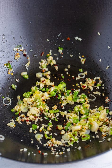 A wok with garlic, green onions, and red pepper flakes.