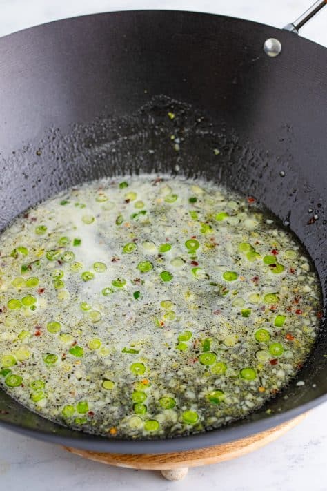 A wok with green onion, garlic, ginger, lemon juice, water, sugar, salt and pepper.