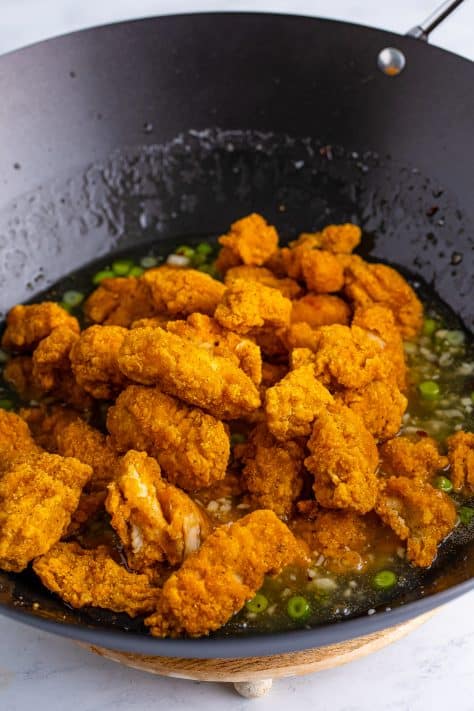 Popcorn chicken being added to a wok with other ingredients.