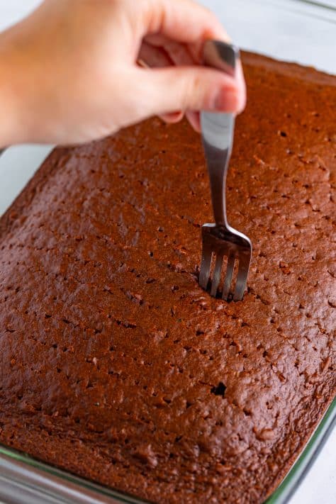 A fork poking holes in a devils food chocolate cake.