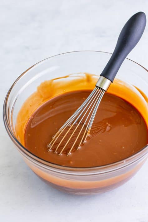 Sweetened condensed milk and chocolate syrup mixed together in a mixing bowl with a whisk.