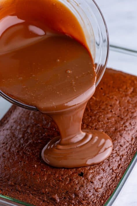 A chocolate syrup sauce being poured on a chocolate cake.