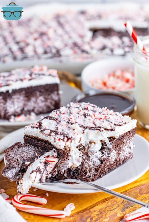 A fork holding a bite of Peppermint Poke Cake next to a slice on a plate.