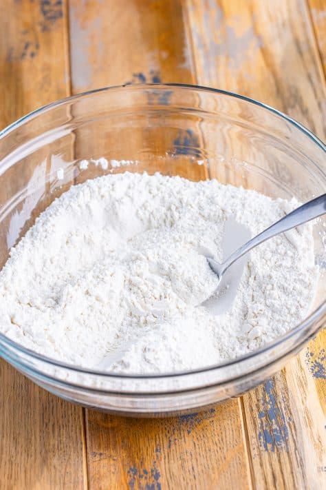A glass mixing bowl of flour, sugar and baking powder.