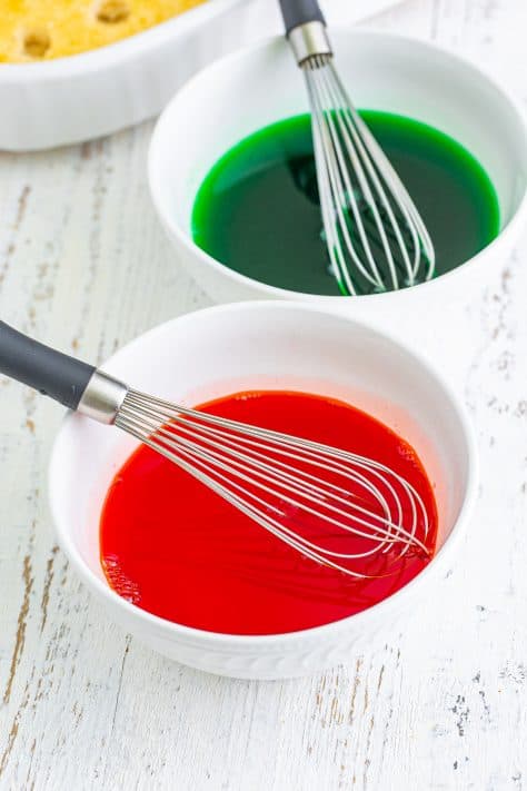 Red and green jello in bowls with whisks.