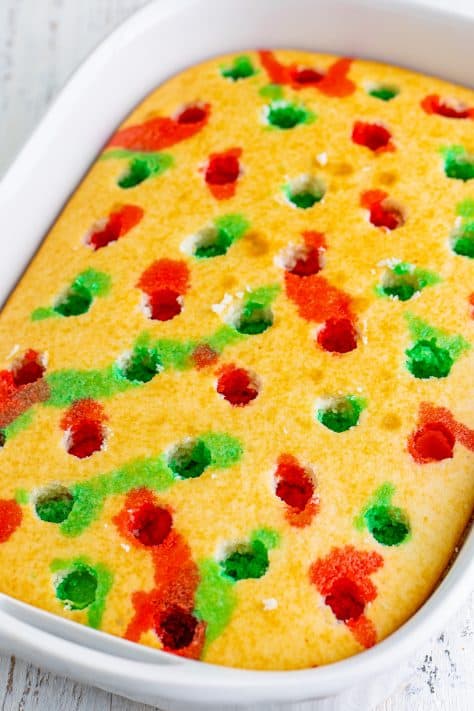 A cake with holes poked in it, filled with red and green jello.