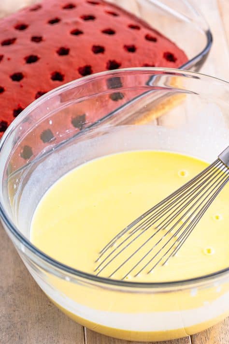 A glass bowl with vanilla pudding mix and milk being whisked together with the whisk in the bowl.