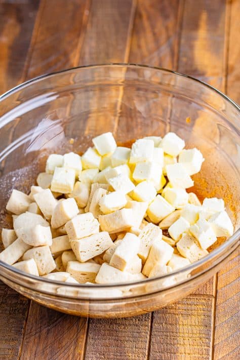 A mixing bowl with brown sugar mixture, cream cheese, and cut up biscuit pieces.