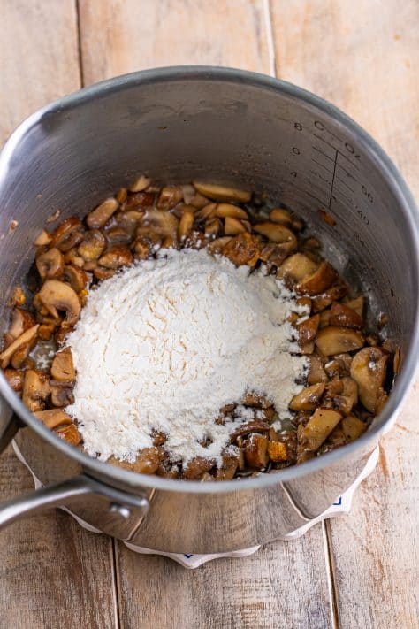 Flour on top of spiced mushrooms in a pot.