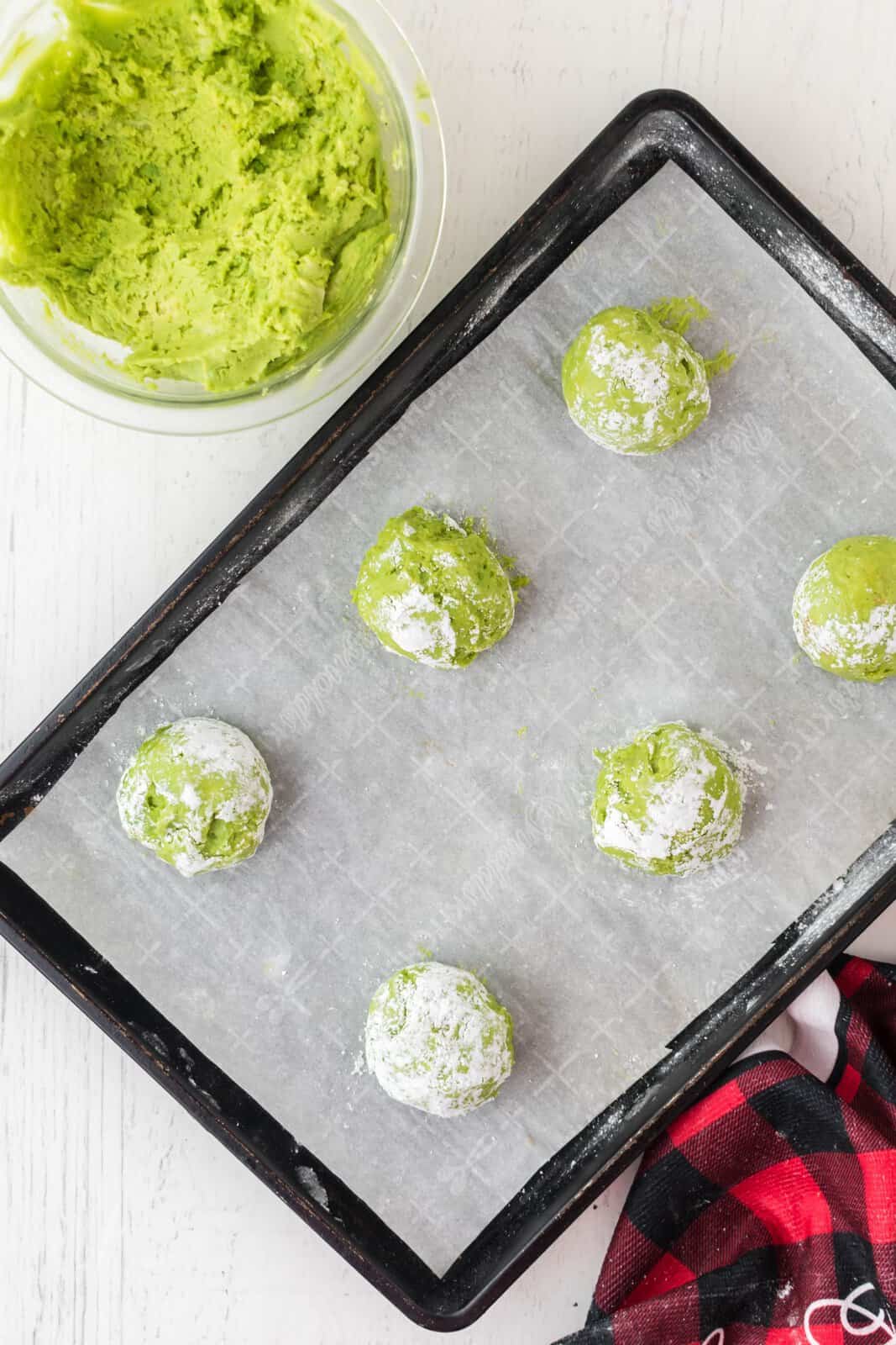 Green cookie dough balls covered with powdered sugar.