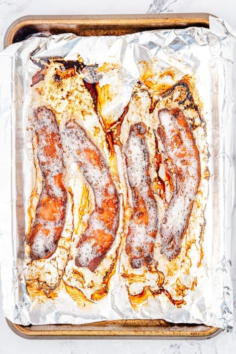 Cooked bacon on an aluminum foil lined baking sheet.