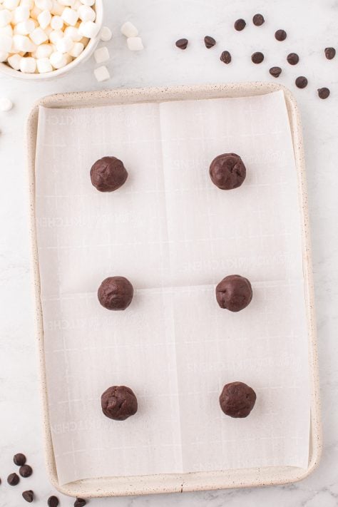 Hot cocoa cookie balls on a lined baking sheet.