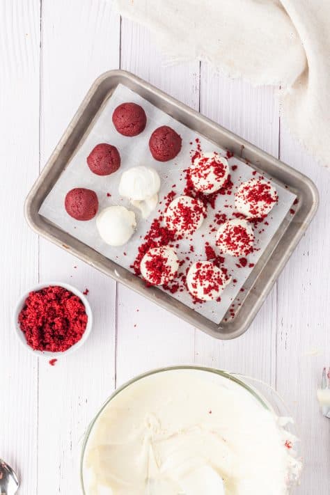 A baking sheet with some red velvet cake balls in a cream cheese frosting.