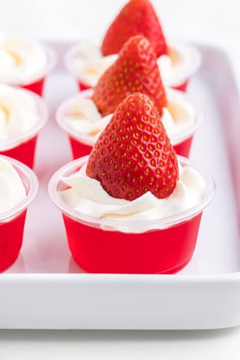 A strawberry on top of whipped cream on top of jello shots.