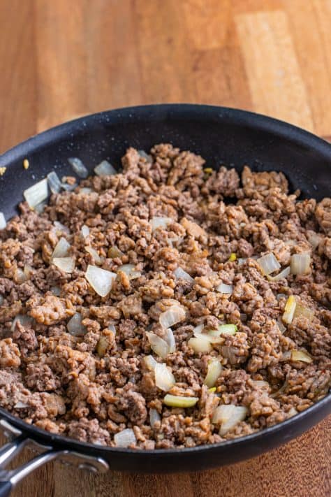 A skillet with onion, ground beef and sausage.