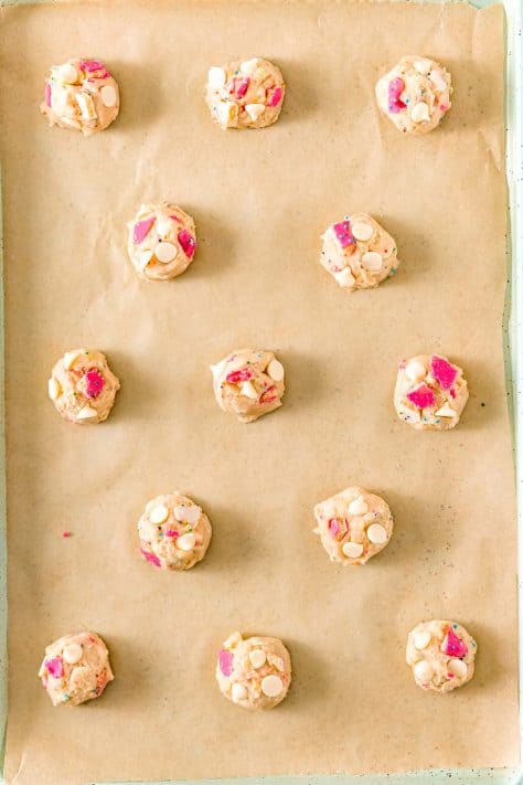 Cookie dough balls on a lined baking sheet.