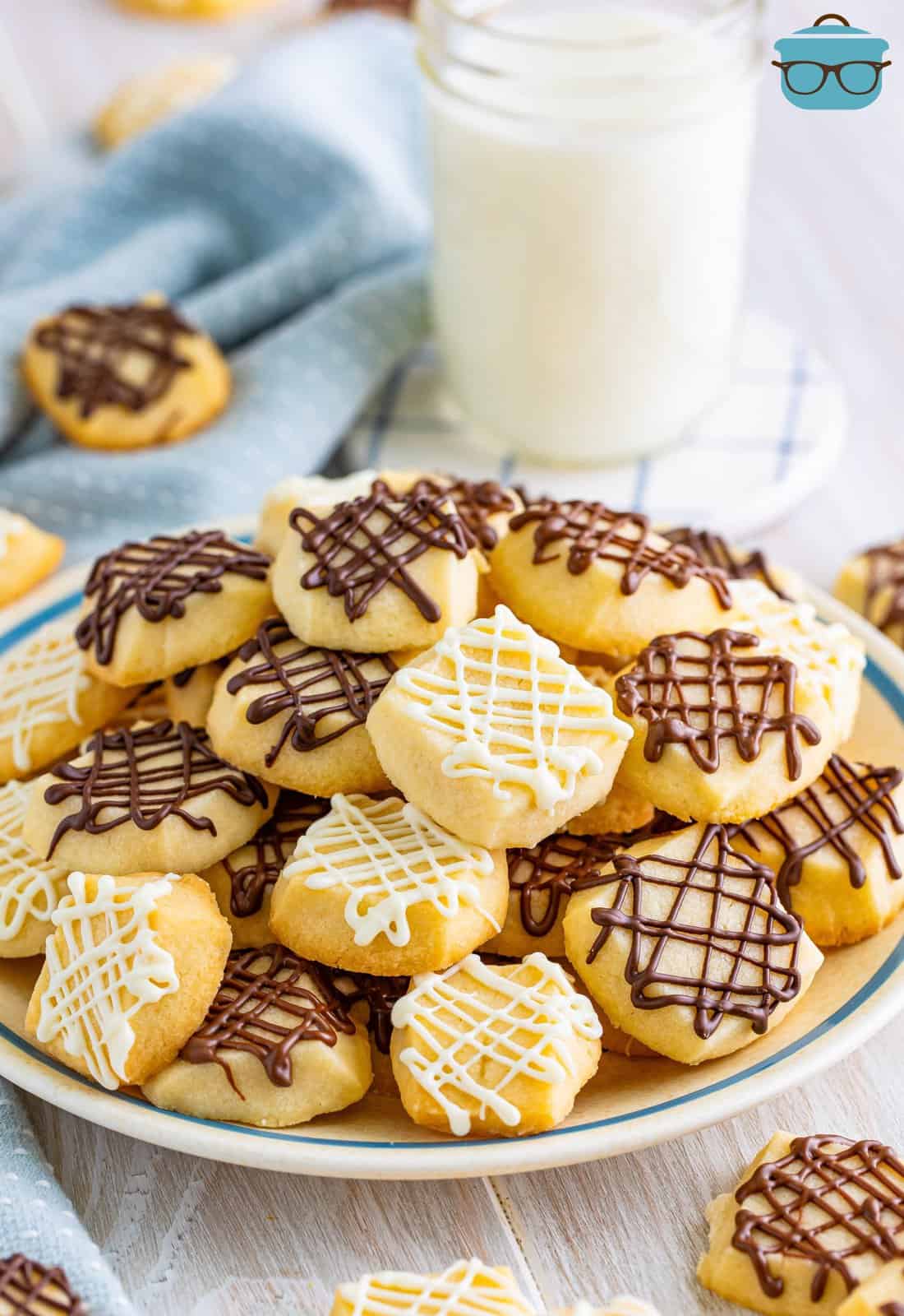 A plate of chocolate drizzled shortbread cookies with a glass of milk.