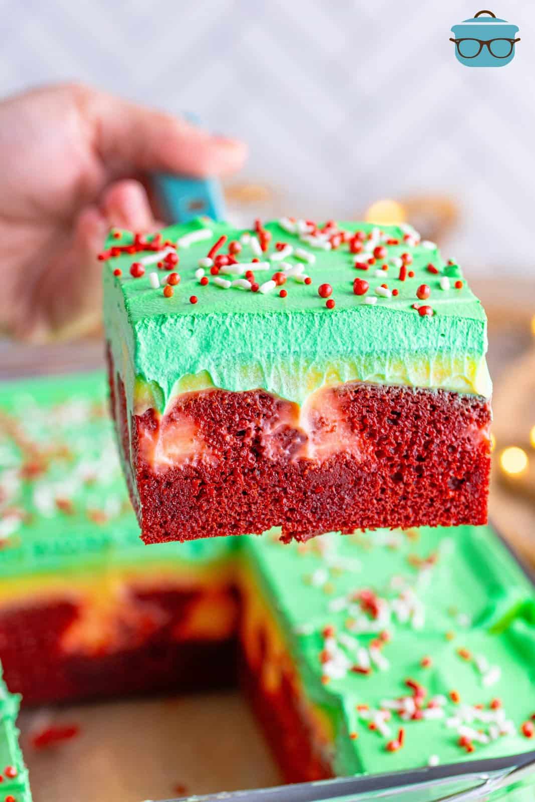 A slice of Christmas Jell-o Poke Cake being lifted above the rest of the cake.