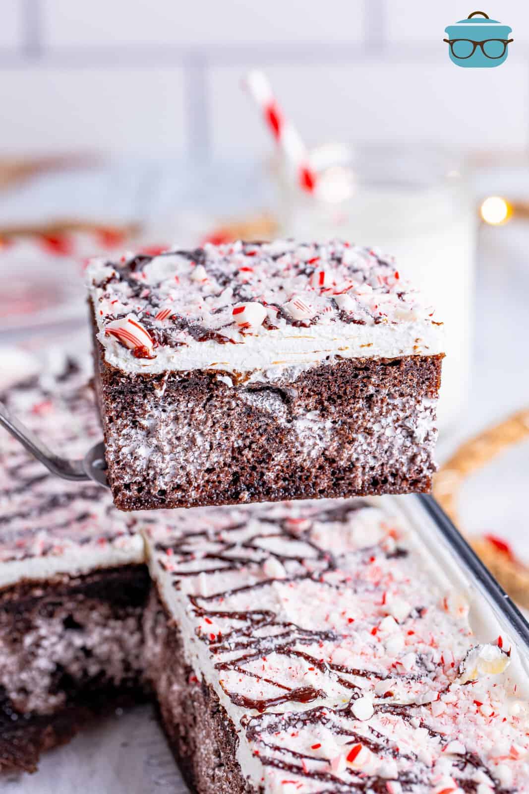 A slice of Peppermint Poke Cake held over the rest of the poke cake by a serving utensil.