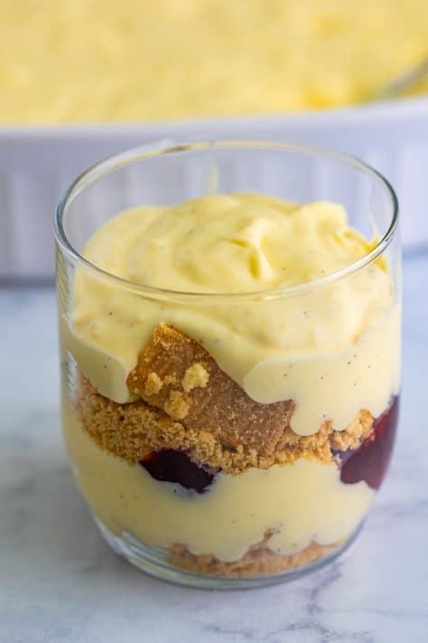 A layered trifle in a glass with custard, cookies, and jam.