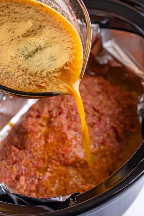 Gravy being poured on uncooked meatloaf.