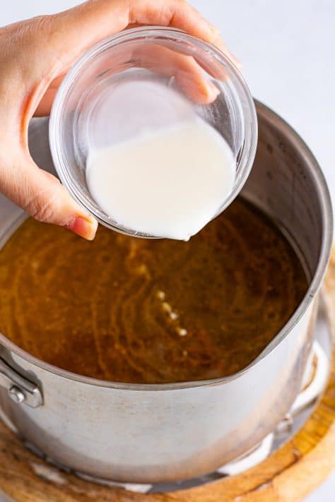Cornstarch slurry being poured in a gravy mixture.