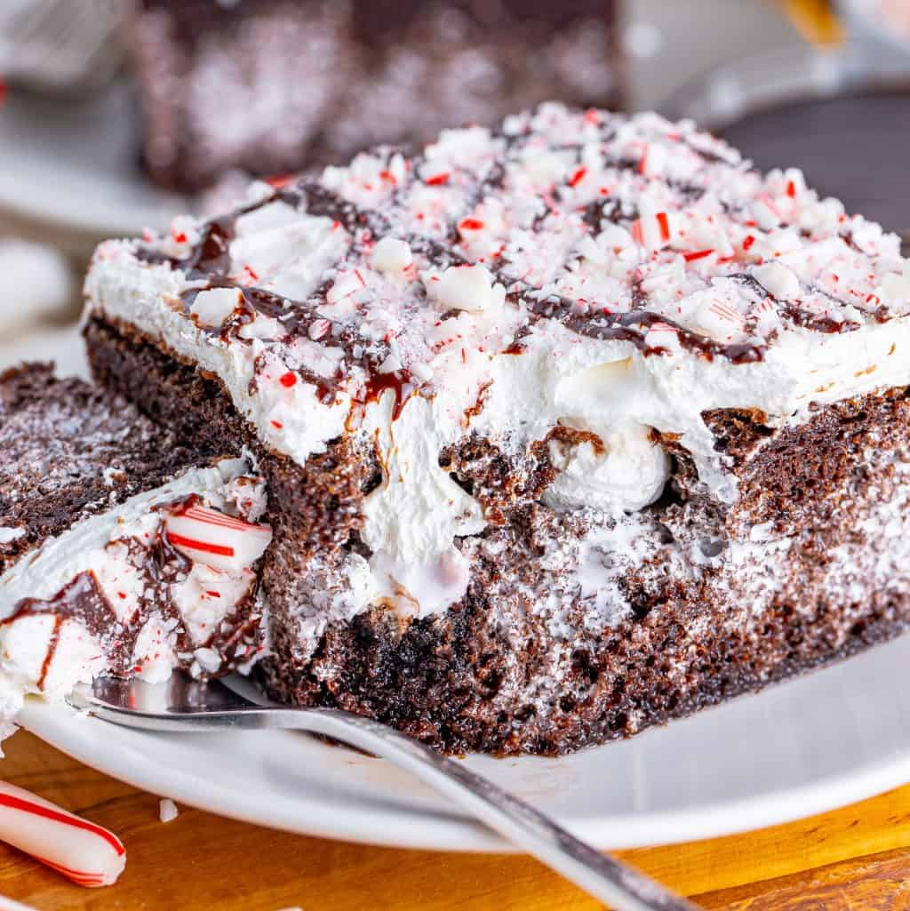 A plate with a slice of Peppermint Poke Cake with a fork holding a bite.