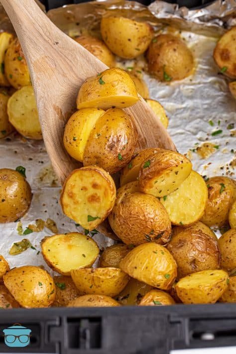 A wooden spoon moving some Air Fryer Lemon Herb Potatoes.